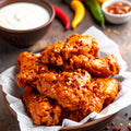 Homemade crispy hot chicken wings coated in fiery chilli sauce, topped with chilli flakes, served with creamy dip and fresh chillies on rustic background
