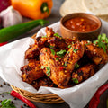 Homemade crispy fajita chicken wings coated in smoky spiced seasoning, topped with fresh coriander, served with salsa dip, peppers and garlic on rustic background