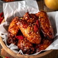 Homemade crispy Korean BBQ chicken wings coated in sticky sweet and spicy glaze, topped with chilli flakes and sesame seeds, served in wooden bowl with fresh chillies on rustic table