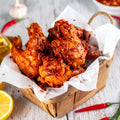 Homemade crispy peri peri chicken wings coated in spicy chilli and garlic marinade, topped with chilli flakes, served with lemon wedge and fresh chillies on rustic wooden table