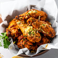Homemade crispy tikka masala chicken wings coated in rich spiced curry marinade, topped with crispy onions and fresh herbs, served in bowl on light background